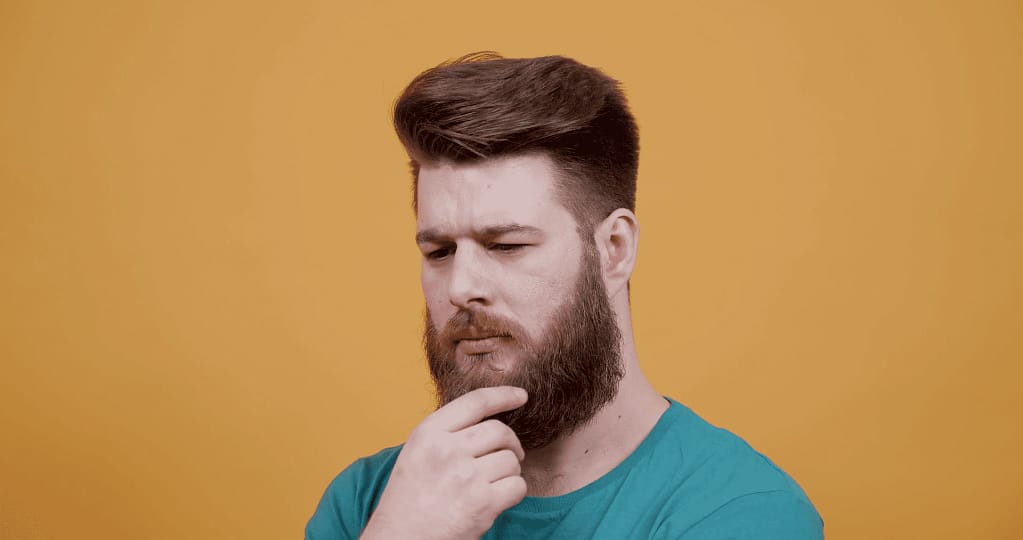 Homem com a mão na barba pensando se deve ter barba ou não