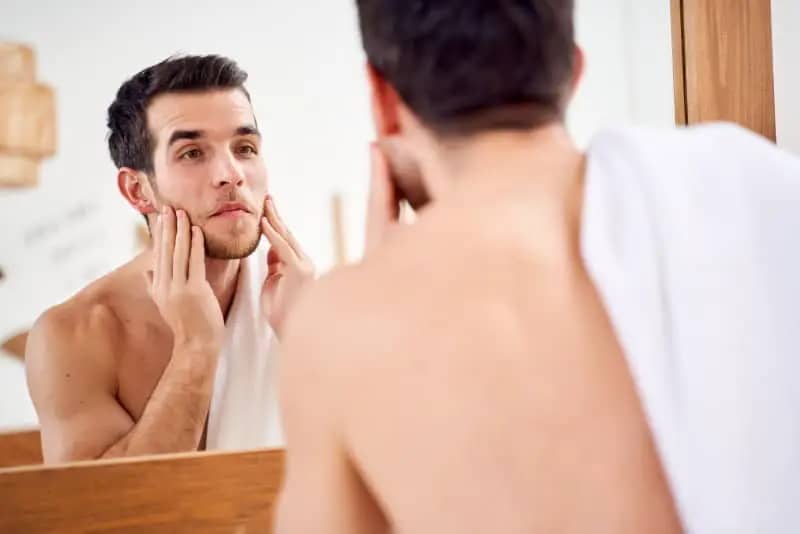 homem olhando para o espelho com a mao na barba